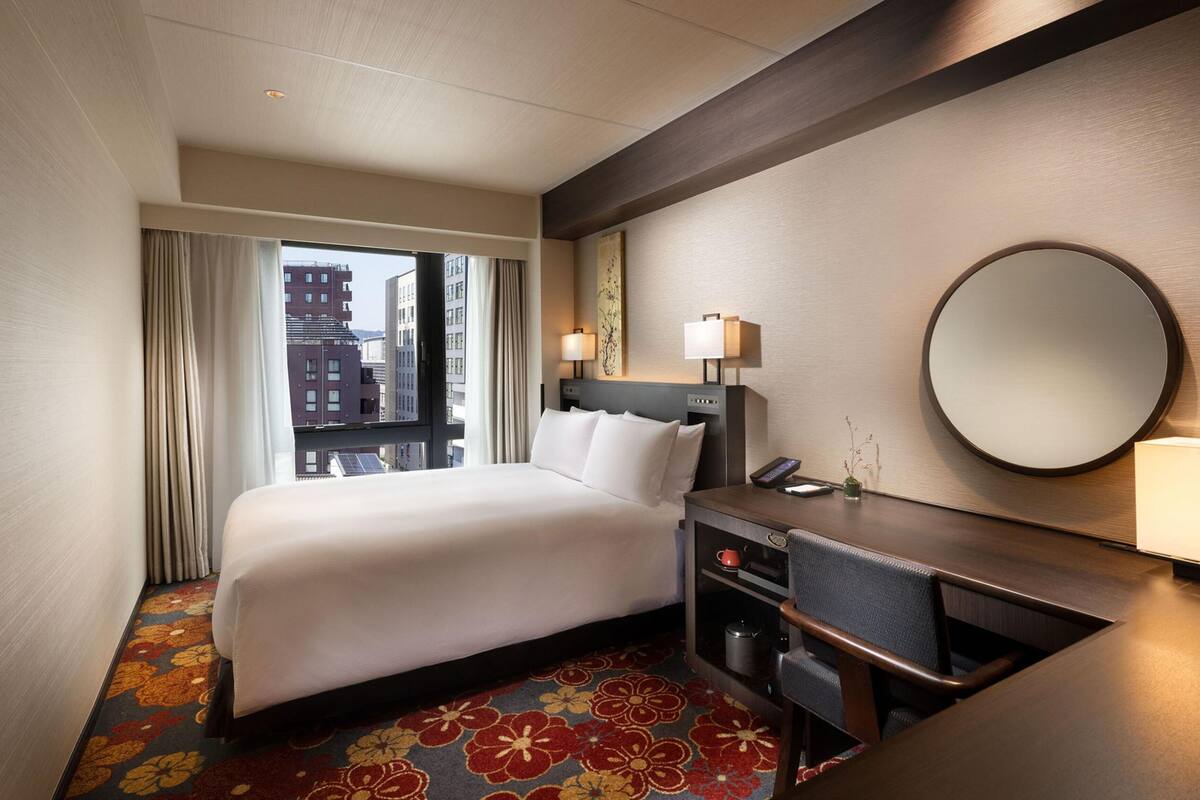 Una camera d'albergo con un letto, una scrivania, uno specchio e vista sugli edifici.