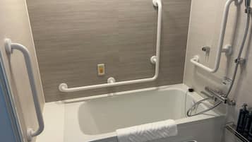 A modern bathroom with a bathtub, grab bars, a handheld showerhead, and a towel rack.