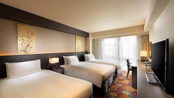 A hotel room with three beds, a desk, a TV, and artwork on the walls.