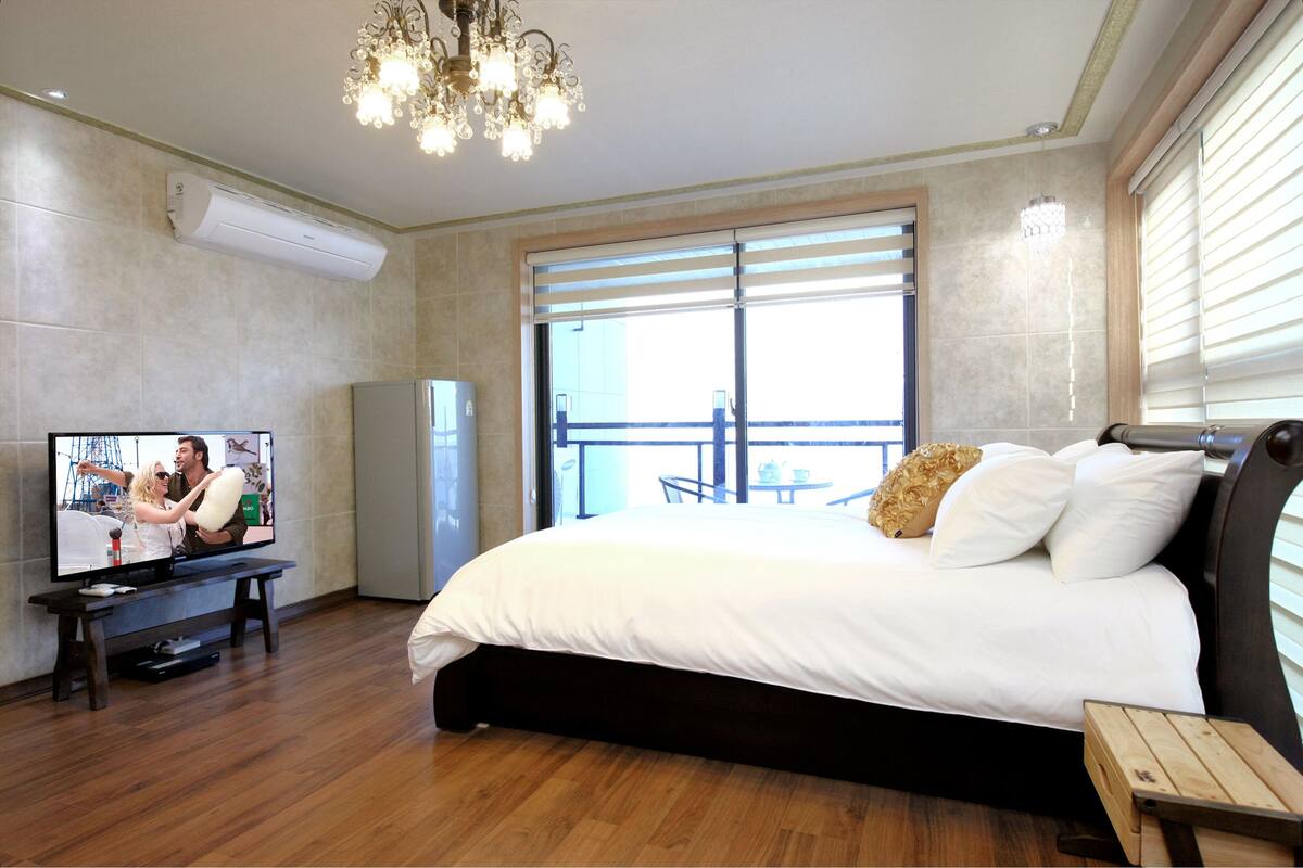 Ein modernes Hotelzimmer mit einem großen Bett, einem Fernseher auf einem Tisch, einer Chandelüster und einem Balkon mit Blick.