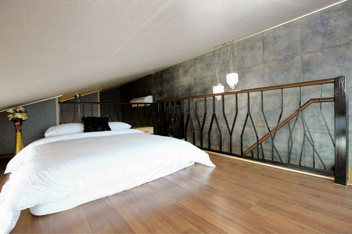 Ein Schlafzimmer mit einem großen Bett, Holzboden, einer dunklen Wand und einem Metallgeländer.