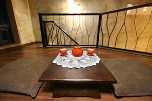 A wooden table with a white lace tablecloth, three orange cups, and a teapot.