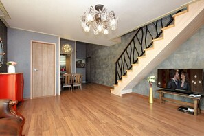 A spacious living room with a wooden staircase, a chandelier, and a television.