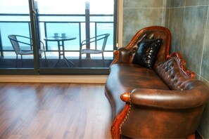 A leather sofa with a decorative pillow, a wooden floor, and a view of the sea through a glass door.