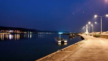 A nighttime harbor scene with calm water reflecting lights, a dock, and a concrete walkway.