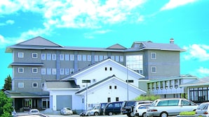 A multi-story building with a prominent entrance, several windows, and a parking area with various vehicles. - Attamari Land Fukabori (Oishida)