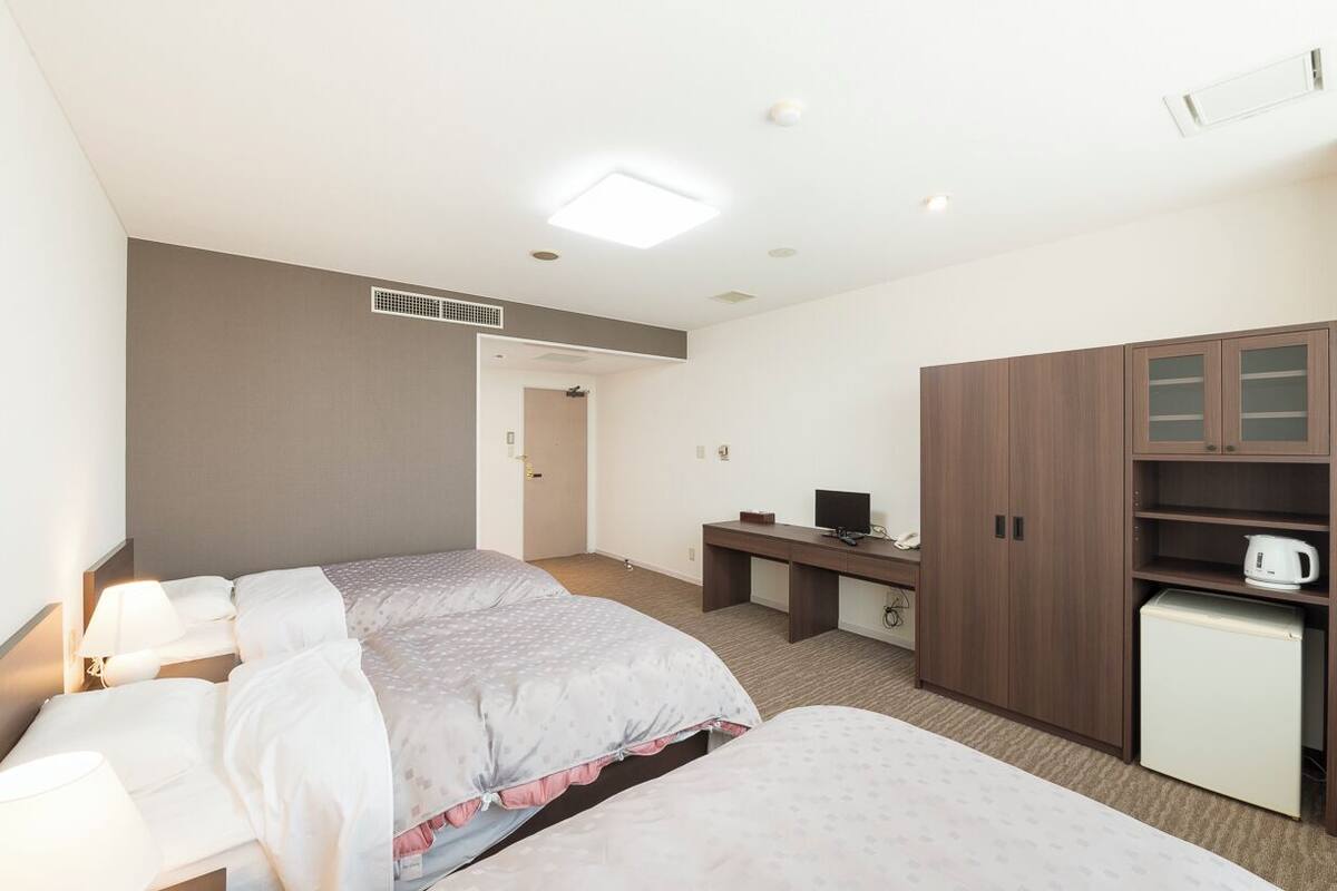 A hotel room with two beds, a desk, a small refrigerator, and a television.
