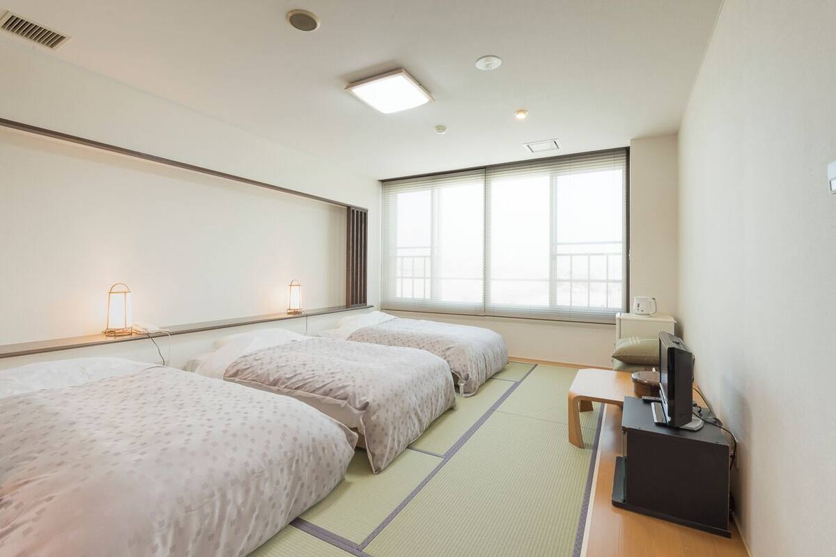 A hotel room with two beds, a desk with a computer, and a window with blinds.