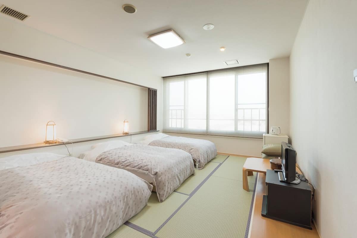 A hotel room with two beds, a desk with a computer, and a window with blinds.