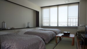 A hotel room with two beds, a small table, a TV, and a window with blinds. - Attamari Land Fukabori (Oishida)