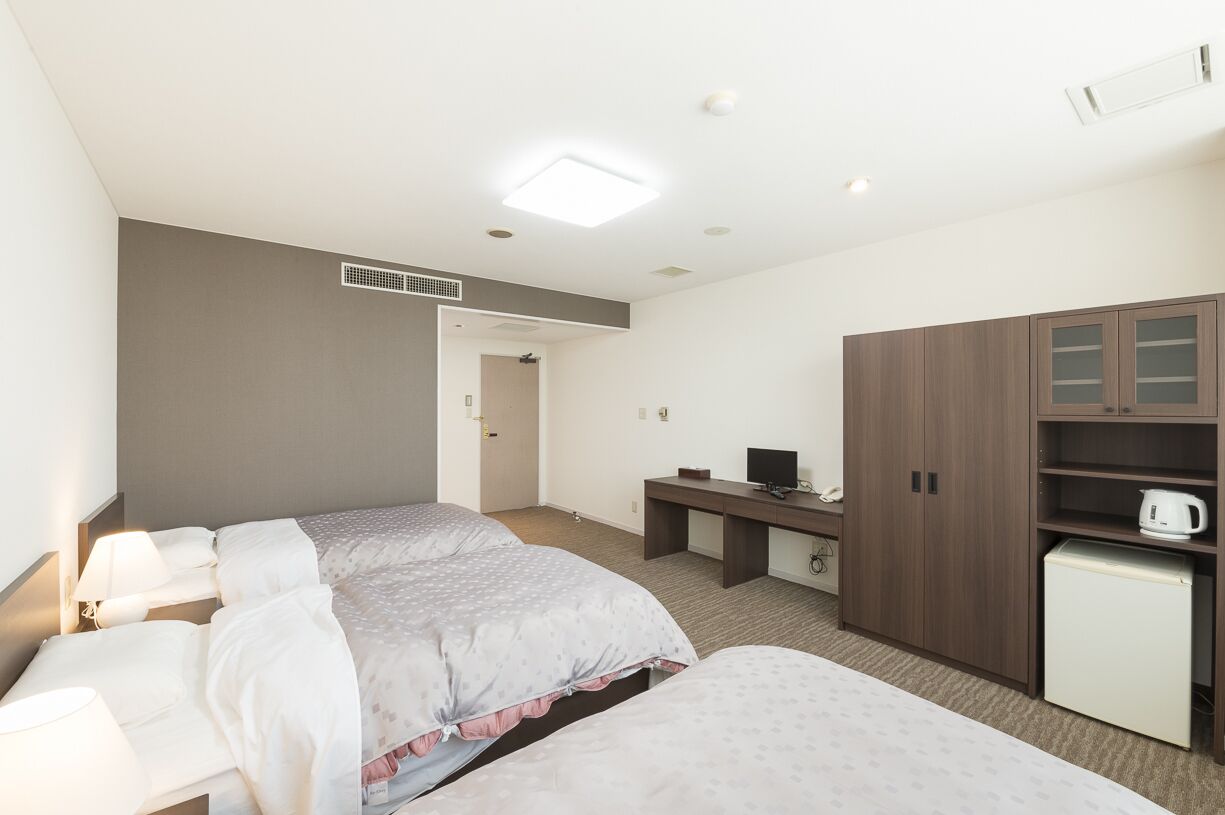 A hotel room with two beds, a desk, a small refrigerator, and a wardrobe.