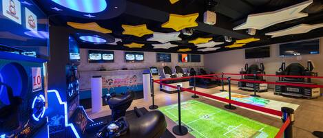 A gaming area with multiple racing simulators, a VR station, and a digital display of a soccer field.