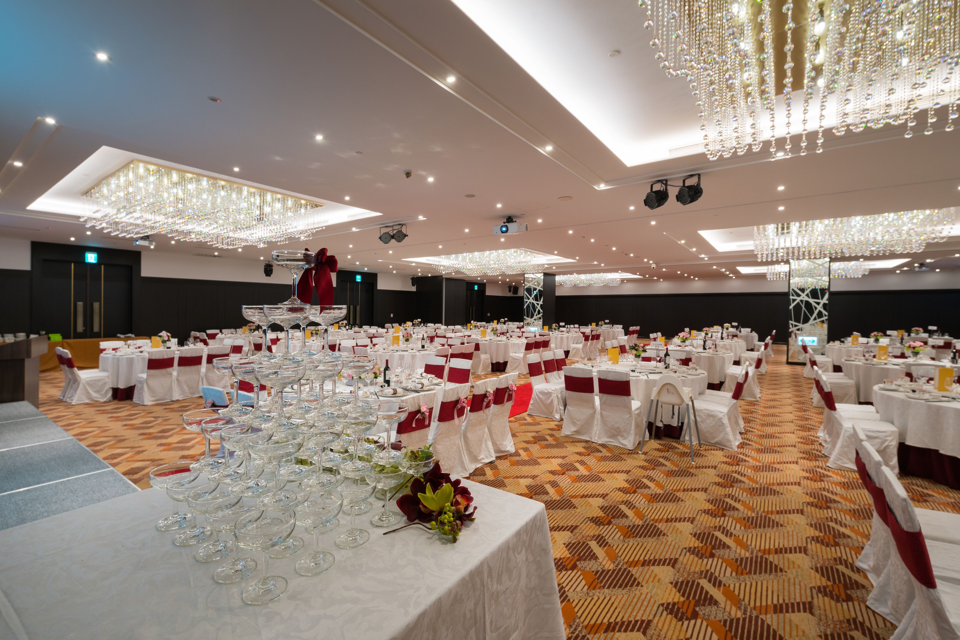 A banquet hall with multiple round tables, each set with white tablecloths and red sashes.
