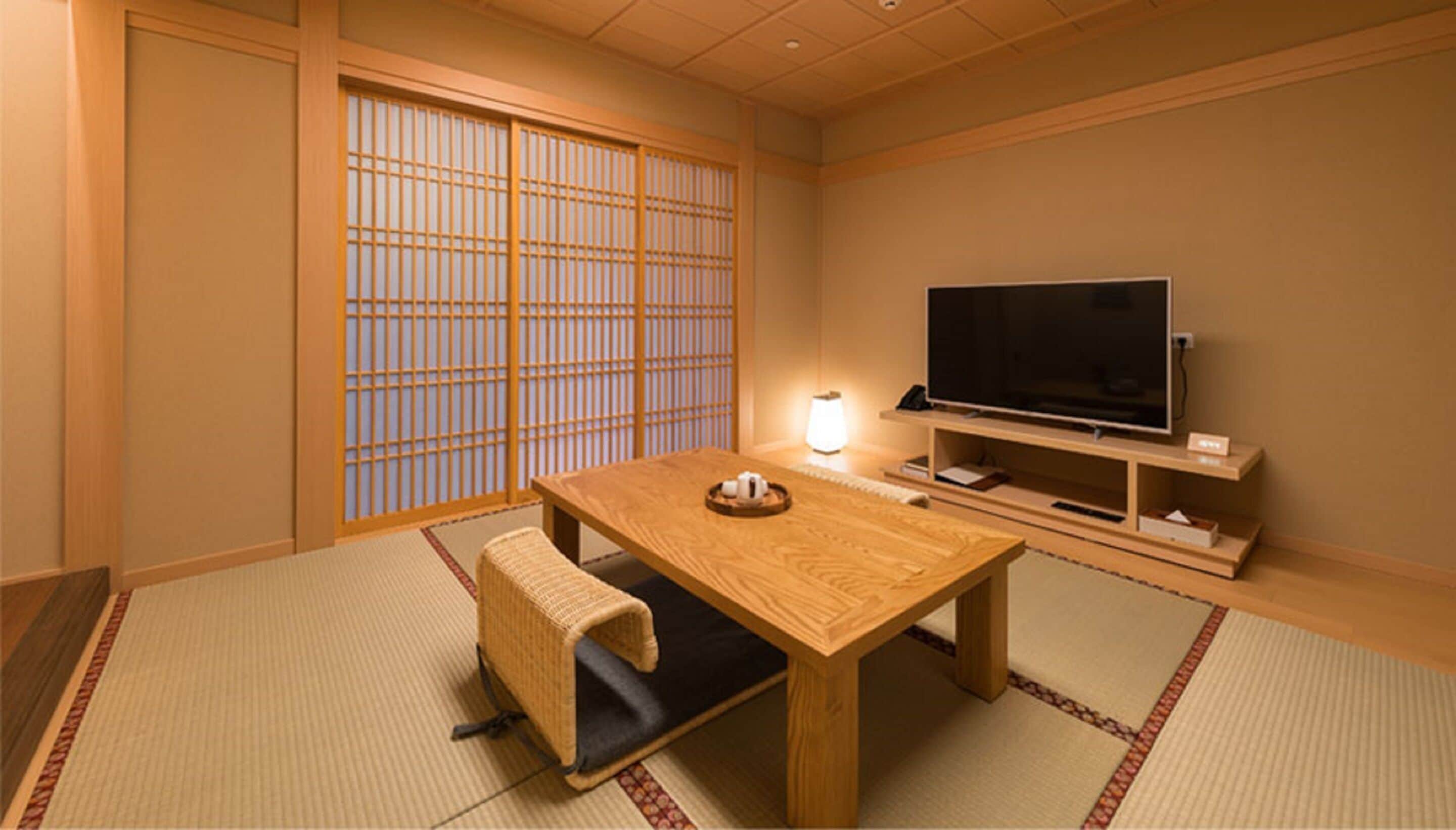 A traditional Japanese room with tatami flooring, a low wooden table, a television on a stand, and sliding shoji doors.