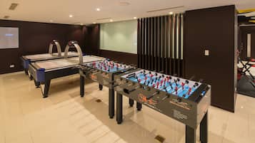 A room with two foosball tables, a projection screen, and a large window with blinds.