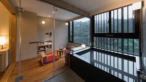 A modern hotel room with a sliding glass door leading to a balcony, a small seating area with a table, and a view of a forested area. - Asia Pacific Hotel Beitou (Taipei)