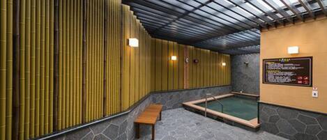 A spa area with a stone floor, wooden benches, a hot tub, and bamboo panels.