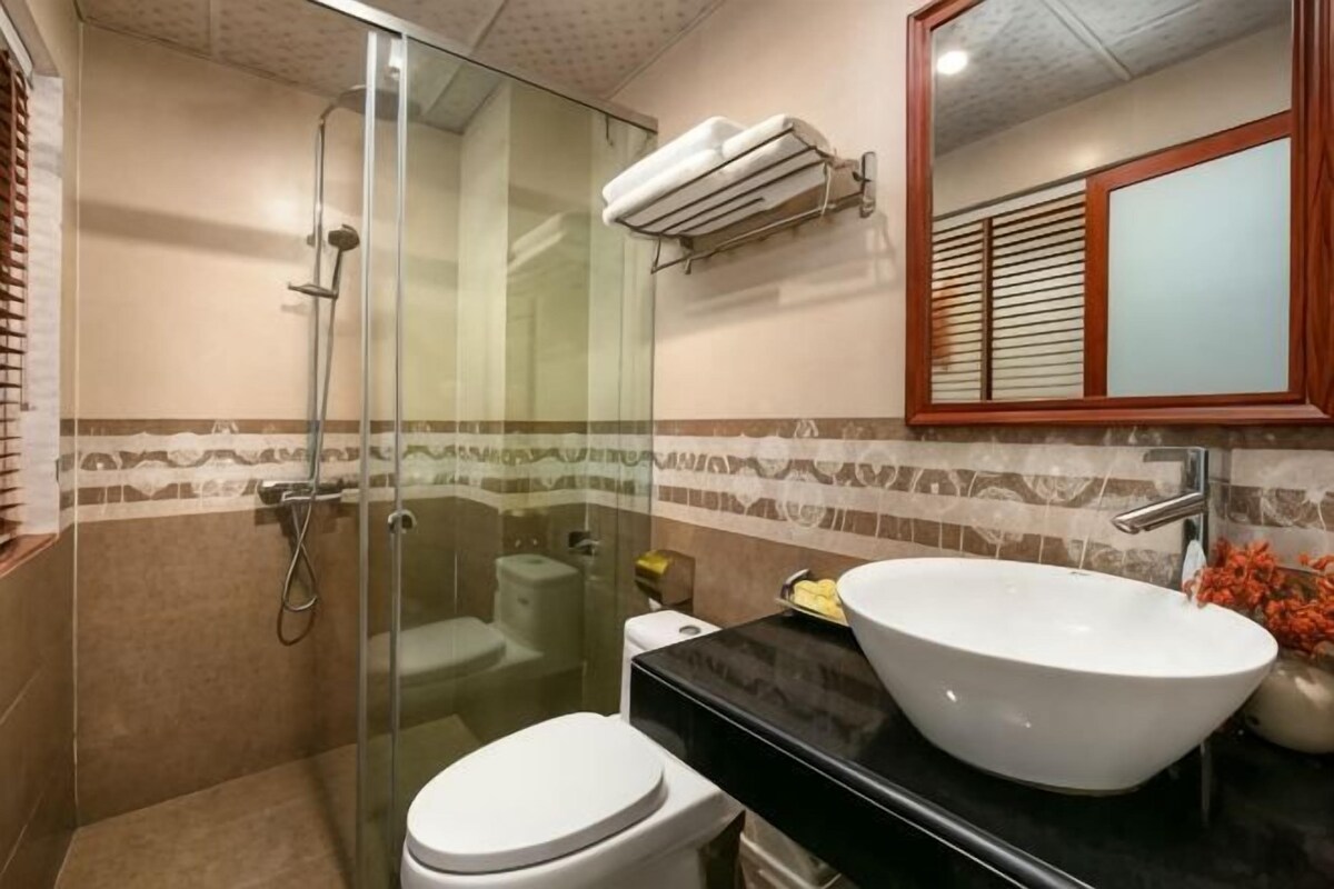 A bathroom with a glass-enclosed shower, a white toilet, a black countertop, a white sink, and a mirror with a wooden frame.