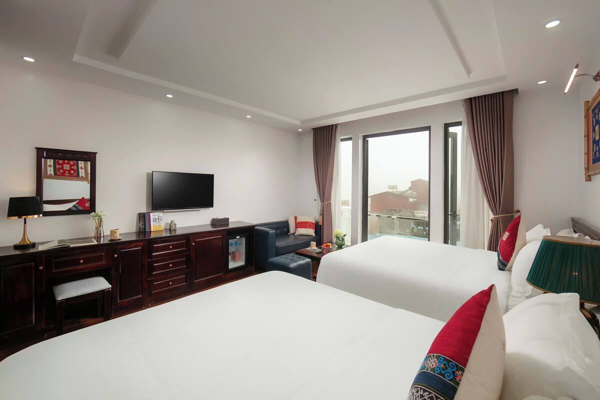 Een hotelkamer met twee bedden, een televisie, een bureau met lades, een zithoekje en een raam met gordijnen.