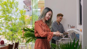 Une femme, vêtue d’une robe à pois, prépare un repas sur le plan de travail de la cuisine.