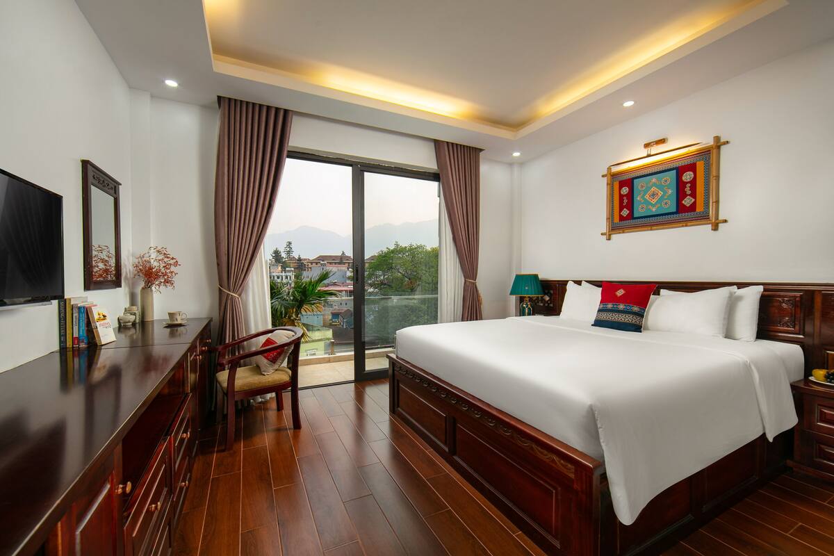 Een hotelkamer met een groot bed, een televisie, een bureau en een balkon met gordijnen.