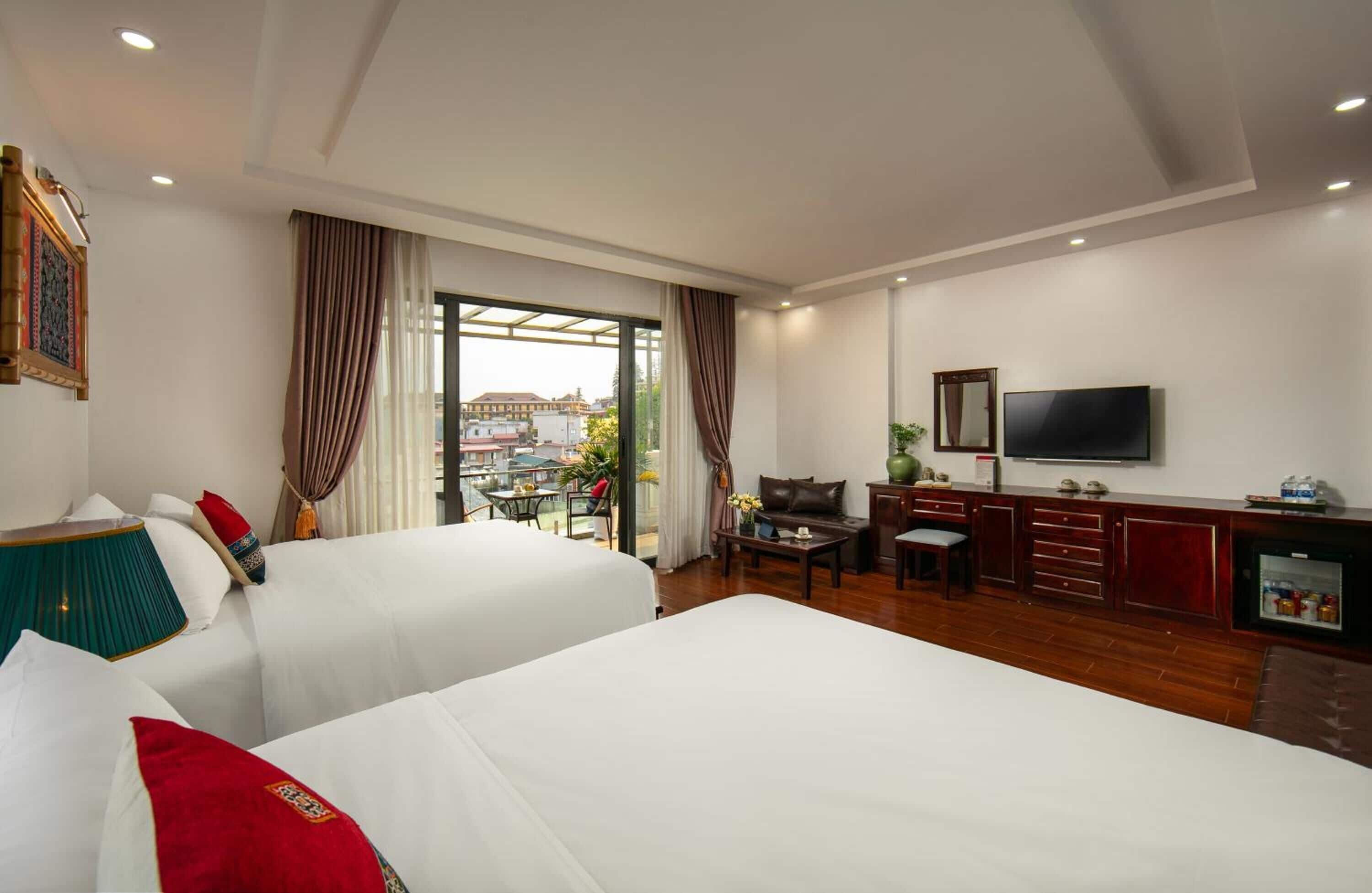 Quarto de hotel com duas camas, uma escrivaninha, televisão e vista para a cidade.