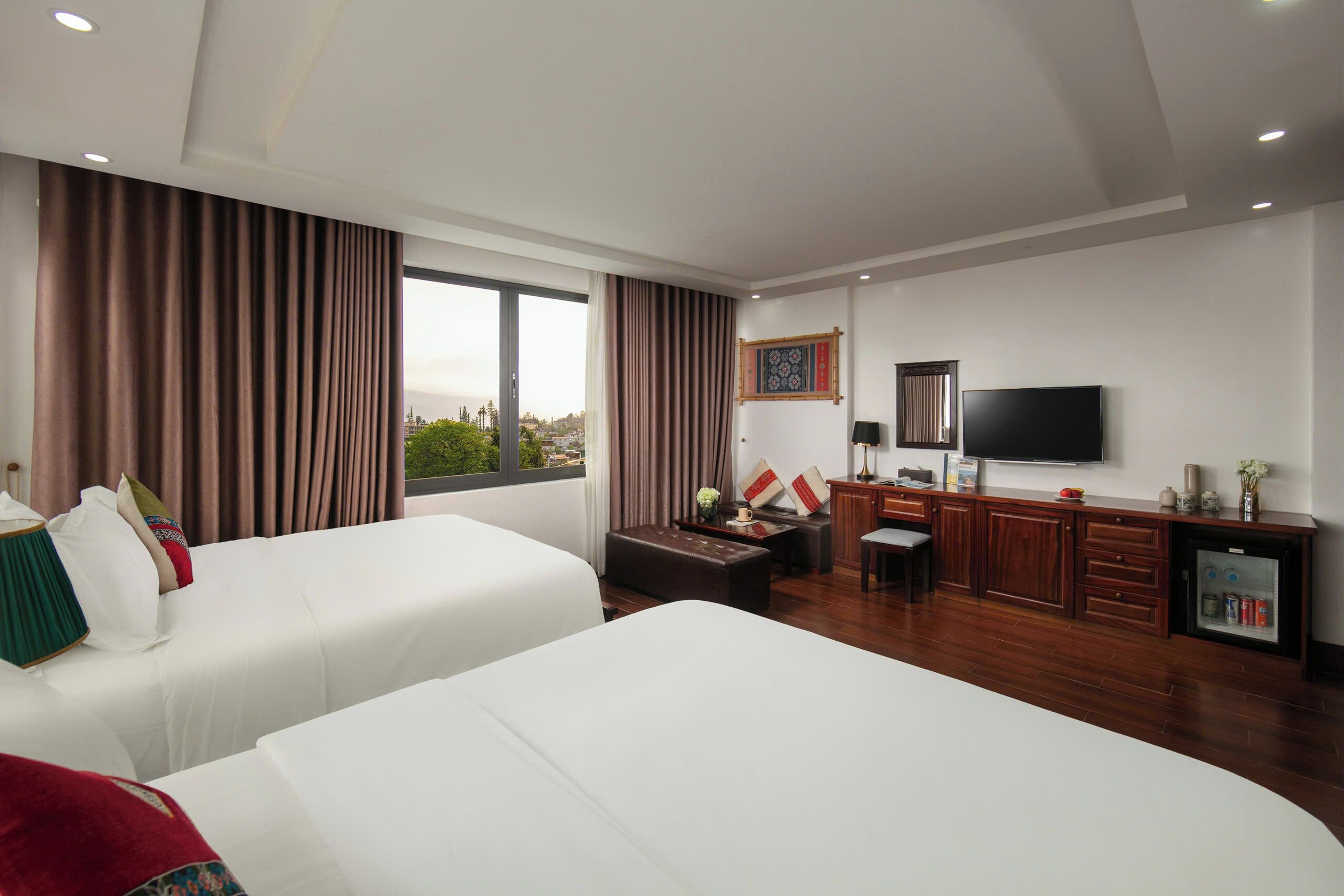 A hotel room with two beds, a desk, a television, and a minibar.
