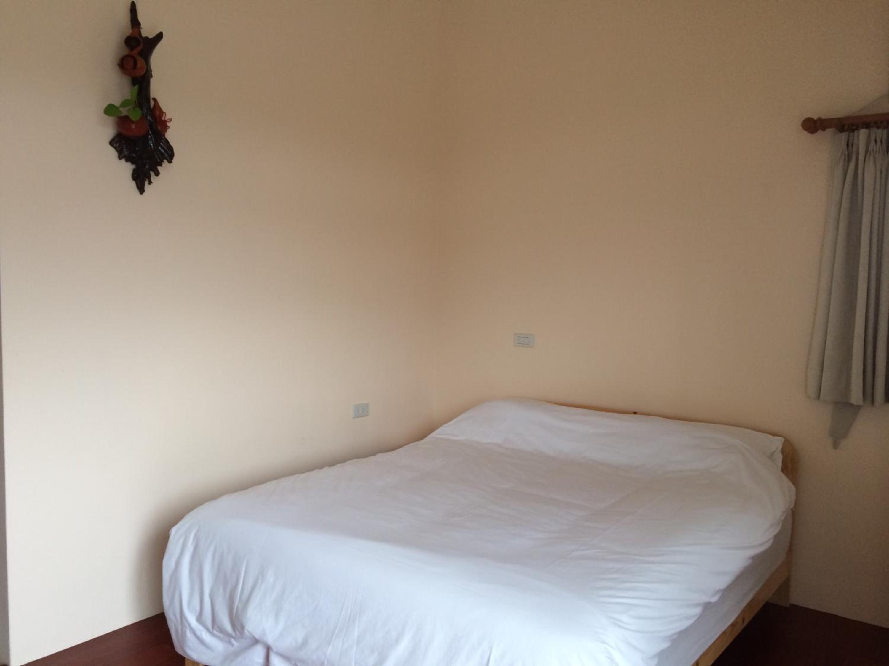 A small, single-bed room with a plain white bedspread, a wooden headboard, and a small wall decoration.