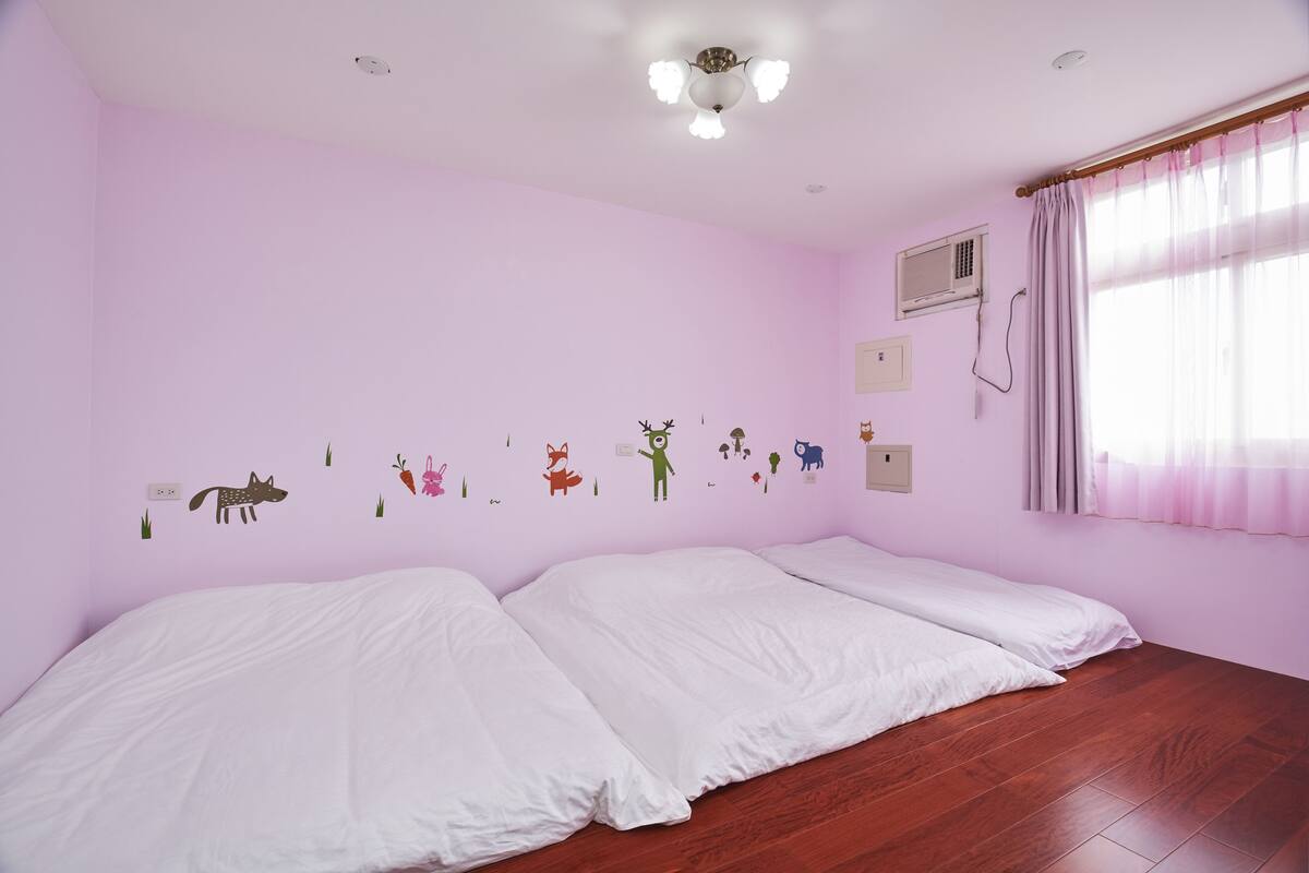 A room with pink walls, two beds, a ceiling fan, an air conditioning unit, and a window with curtains.