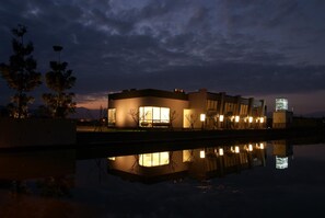 Un bâtiment moderne avec un bassin d’eau réfléchissante à sa base, de grandes fenêtres et un toit plat.