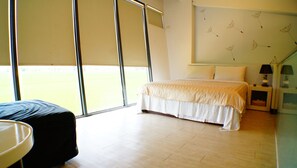 Un dormitorio con cama, mesita de noche, lámpara y vistas a un campo a través de amplias ventanas.