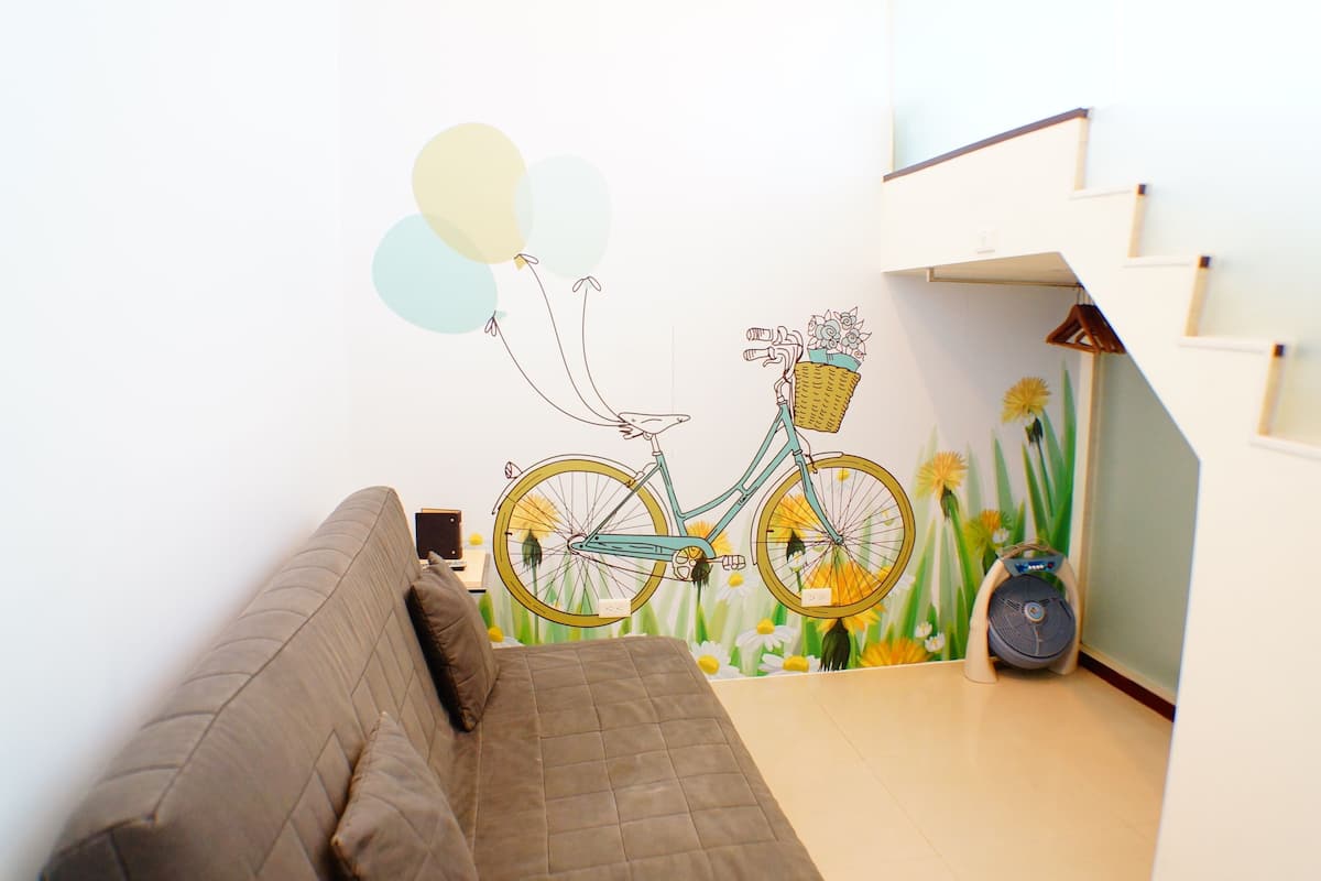 Une pièce avec un canapé marron, une fresque murale représentant un vélo et un escalier.