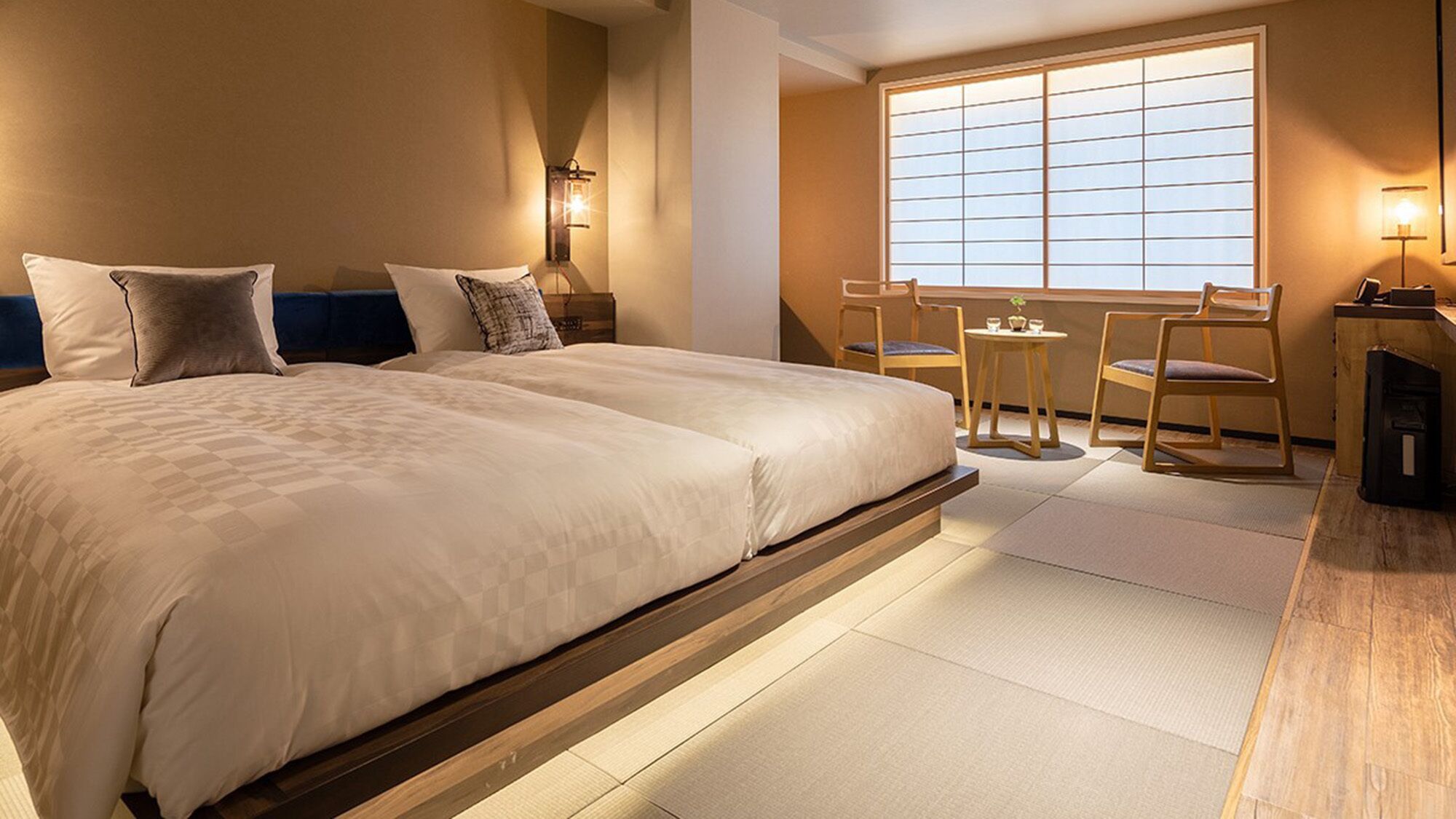 Quarto de hotel com uma cama grande, uma mesinha com cadeiras e vista pela janela.