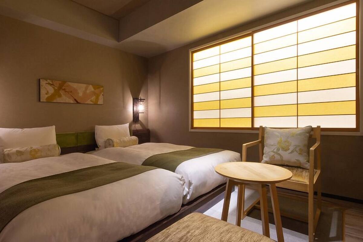 A hotel room with two beds, a chair, a table, and a large window with a view.