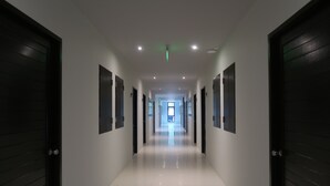 A long, narrow hallway with doors on both sides, leading to a bright room at the end. - Good Morning Hotel at TakuaPa (Takua Pa)