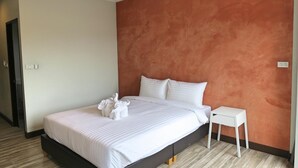 A modern hotel room with a large bed, white linens, a small white nightstand, and a wooden floor. - Good Morning Hotel at TakuaPa (Takua Pa)