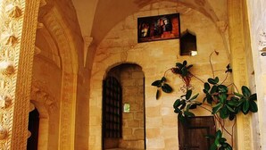 An arched stone doorway with a small window and a door, leading to a room with a blue vase and green plants. - Artuklu Kervansarayi - Special Class (Mardin)