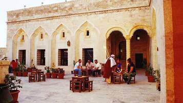 An outdoor courtyard with stone flooring, multiple seating areas, and a building with arched doorways.