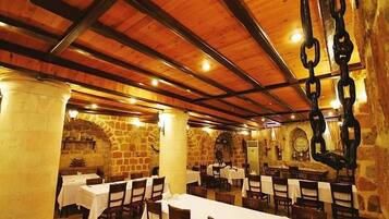 A restaurant with stone walls, wooden beams, and tables set for dining.