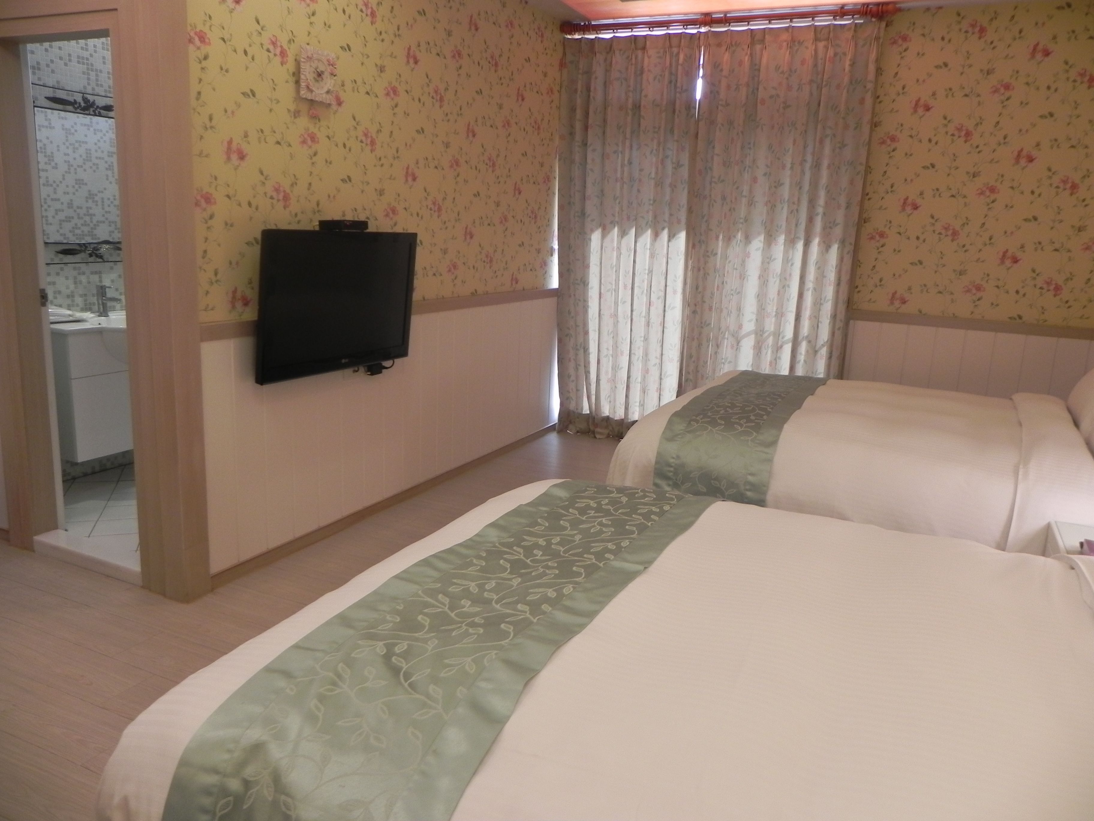 A hotel room with two beds, a television on the wall, and a bathroom visible through an open door.