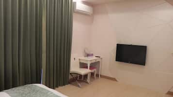 A hotel room with a bed, a desk with a chair, a television mounted on the wall, and a curtain.