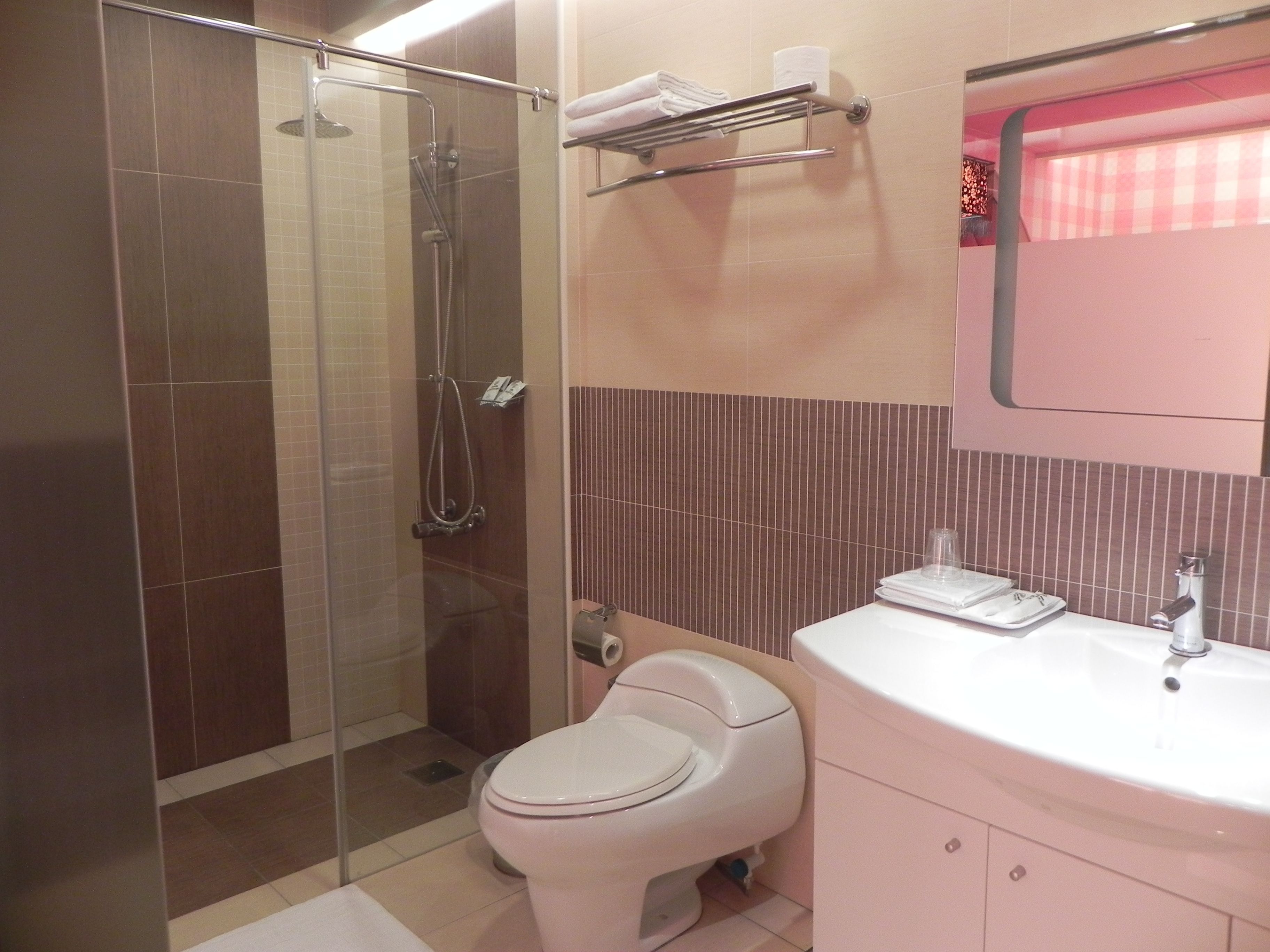 A bathroom with a glass-enclosed shower, a toilet, and a sink with a mirror above it.