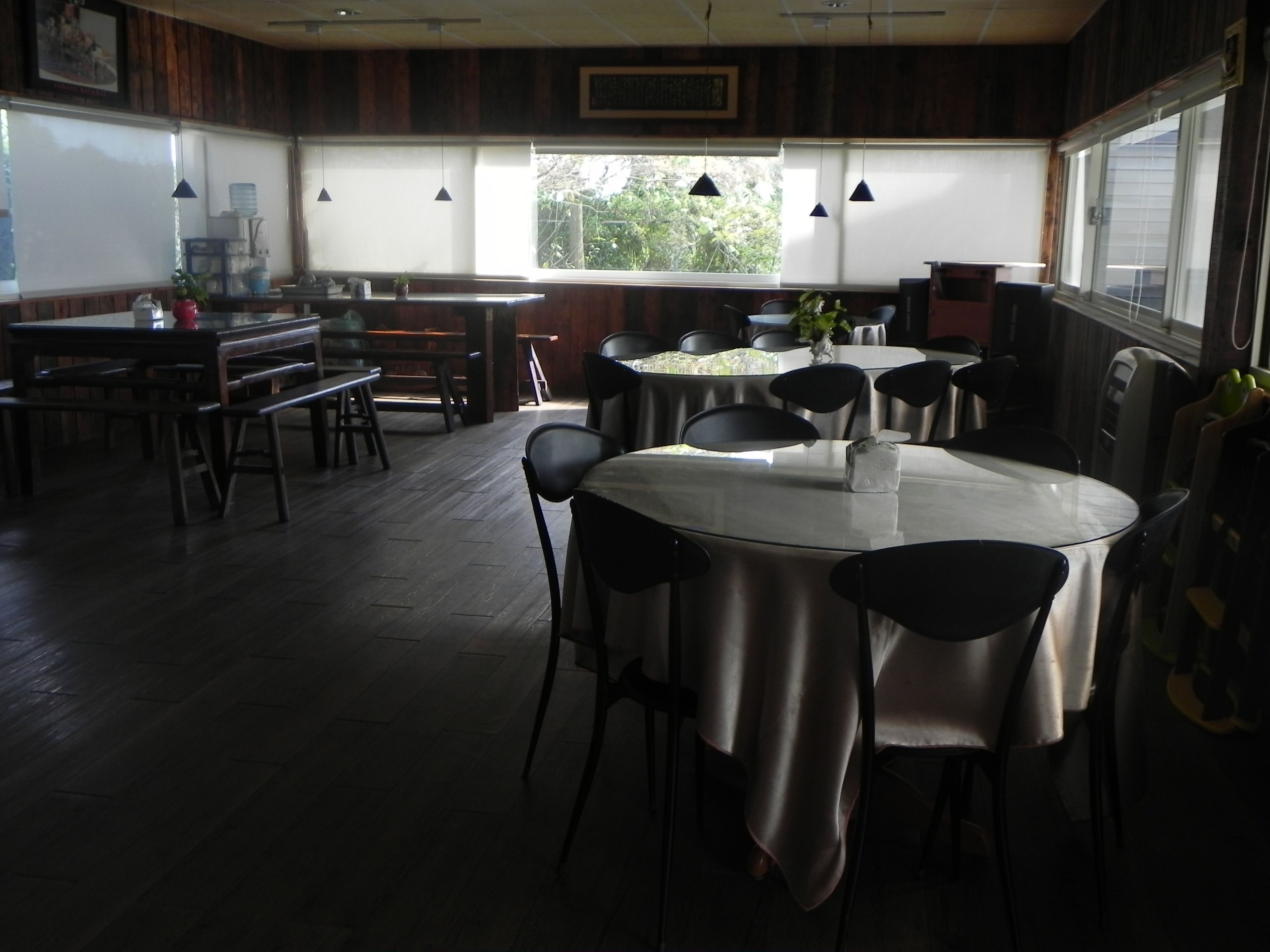 Comedor con mesas y sillas redondas, piso de madera y ventanas grandes que dejan entrar luz natural.