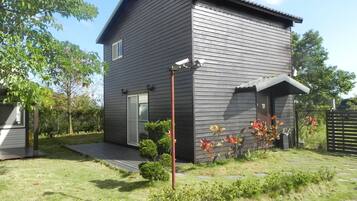 A modern two-story house with a dark exterior, a front porch, and a small garden with flowering plants.