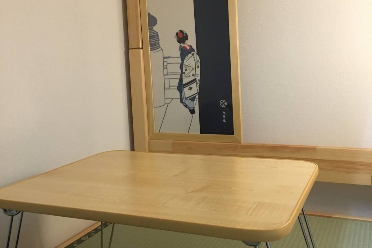 A room with a wooden-framed bed, a small table, and a wall with a traditional Japanese artwork.