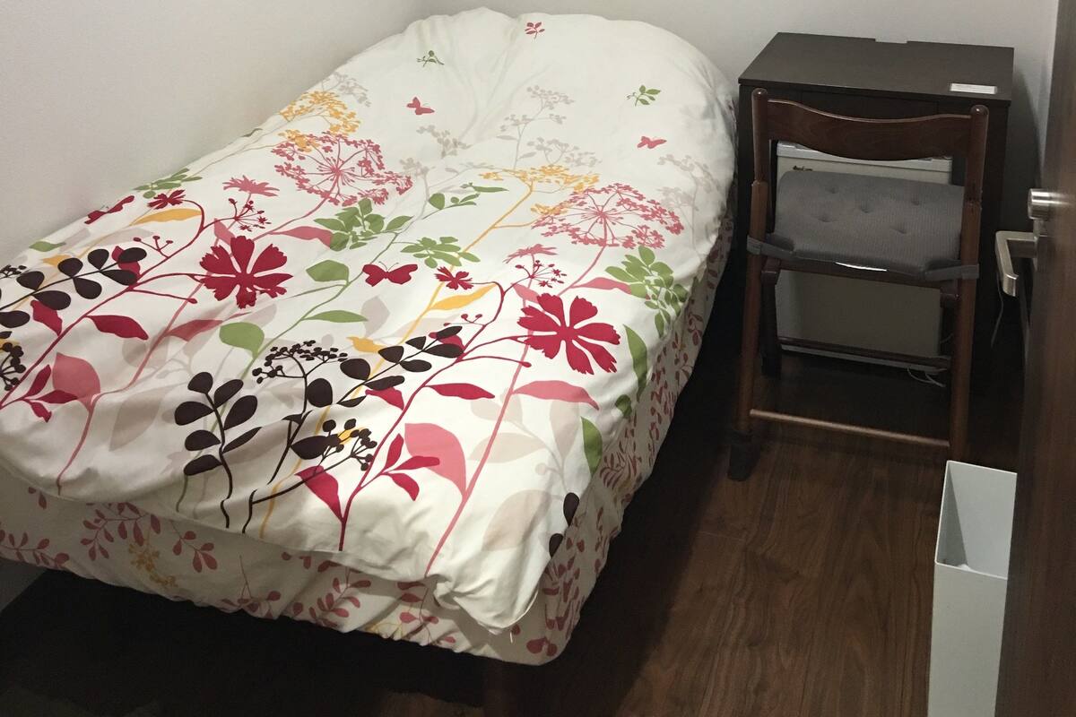 A small, neatly arranged bedroom with a single bed, a nightstand, and a chair.