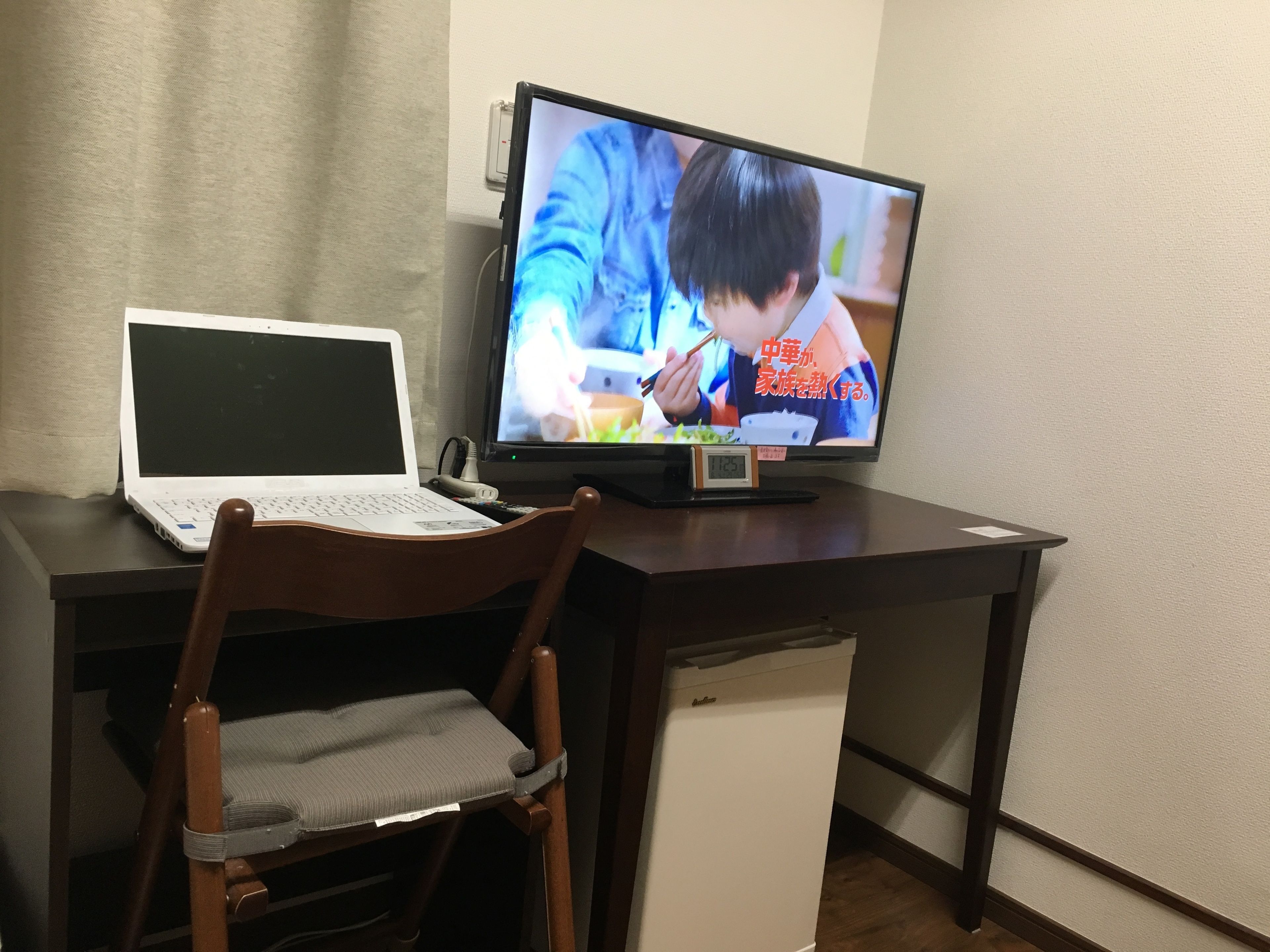 A desk with a laptop, a television, and a chair.