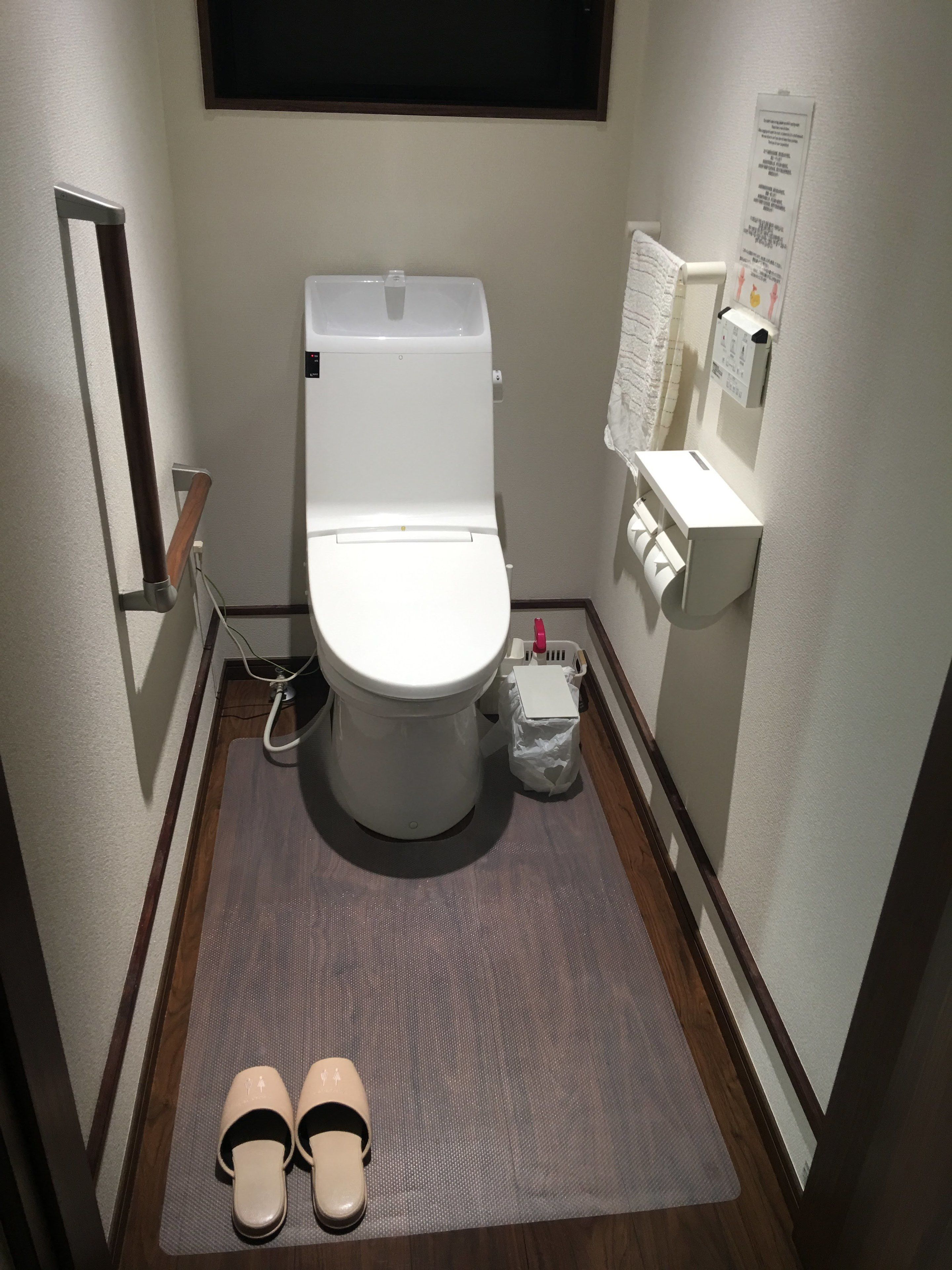 A small, compact bathroom with a white toilet, a small trash bin, and a paper dispenser on the wall.