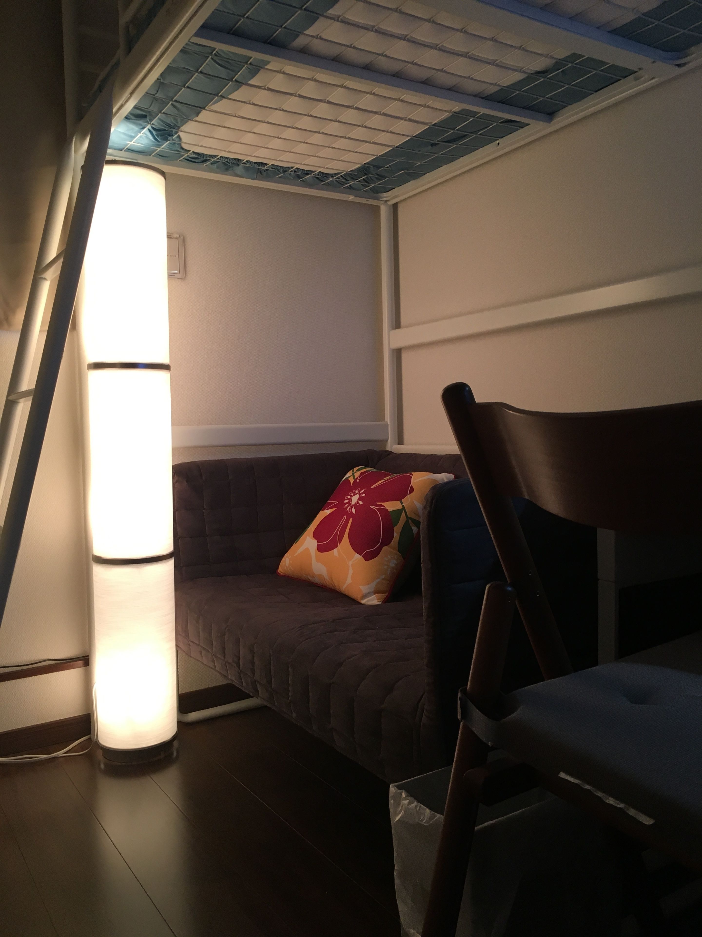 A room with a slanted ceiling, a cushioned bench, a pillow with a floral design, and a standing lamp.