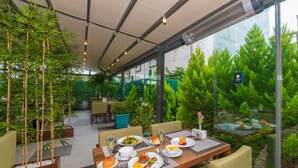 A restaurant with a dining table set for four, surrounded by bamboo plants and a view of a pond with fish. - Land Park Hotel (Istanbul)